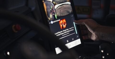 The hand of an operator inside the cab of a Volvo Articulated Hauler accesses media on their smart device