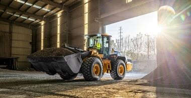 Volvo L120 Electric wheel loader dumping aggregate into an industrial depot building.