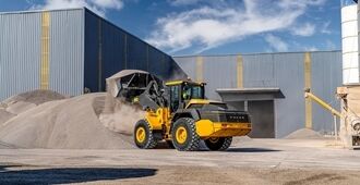 A  Volvo L120H Electric Wheel Loader in motion, lifting materials with its front-mounted bucket in a construction site.