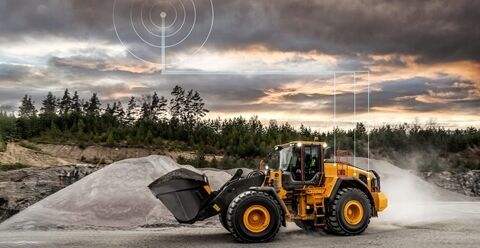 volvo wheel loader L180 loading Volvo truck in a quarry. Connectivity graphic above them shows connection with CareTrack.