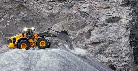 Volvo L180 wheel loader travelling across quarry at speed with full bucket