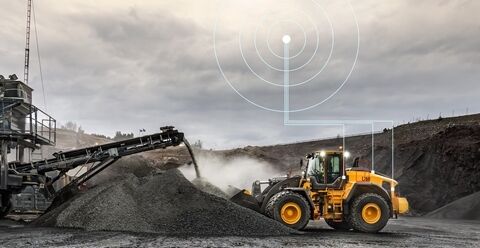 Volvo L260 wheel loader loading a Volvo truck in a quarry with data pulse above both vehicles showing the connectivity with CareTrack