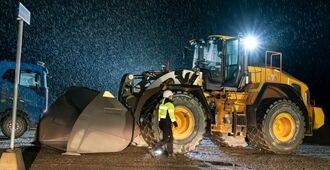 Operator climbing down from Volvo L260 wheel loader at night with lights on